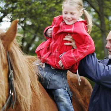 Bedstefar løfter barn op på hest